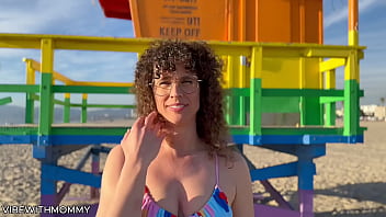 A middle-aged Jewish woman engages in sexual activity with a stranger at the beach, both of them wearing bikinis.